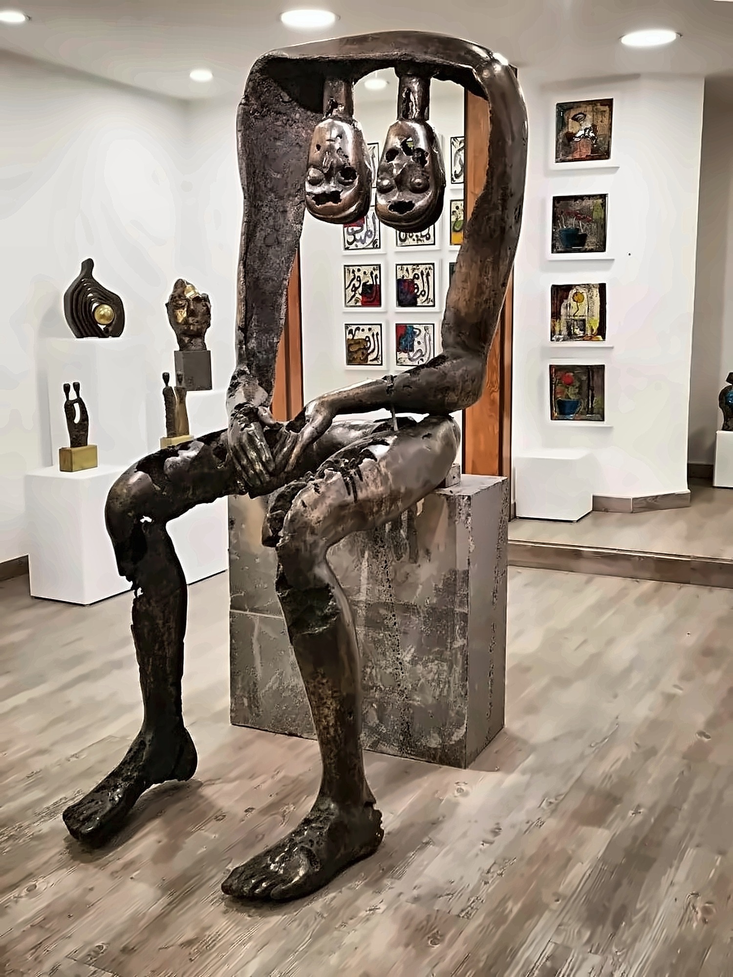 Hazem Al-Zubi’s bronze sculpture Ain Ghazal, showing a seated figure beneath two suspended heads.