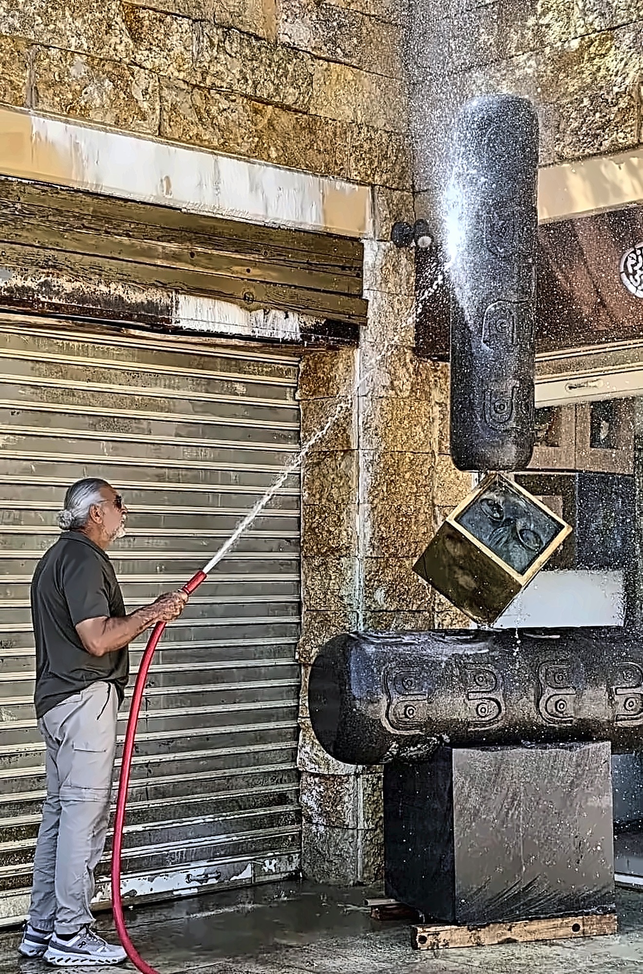 The artist hosing down a tall basalt and bronze sculpture outside his gallery.