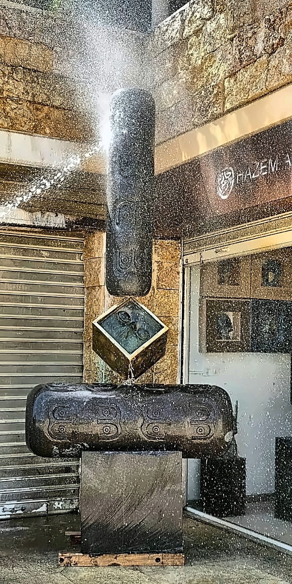 Water breaking over the gilded cube between the two drums.