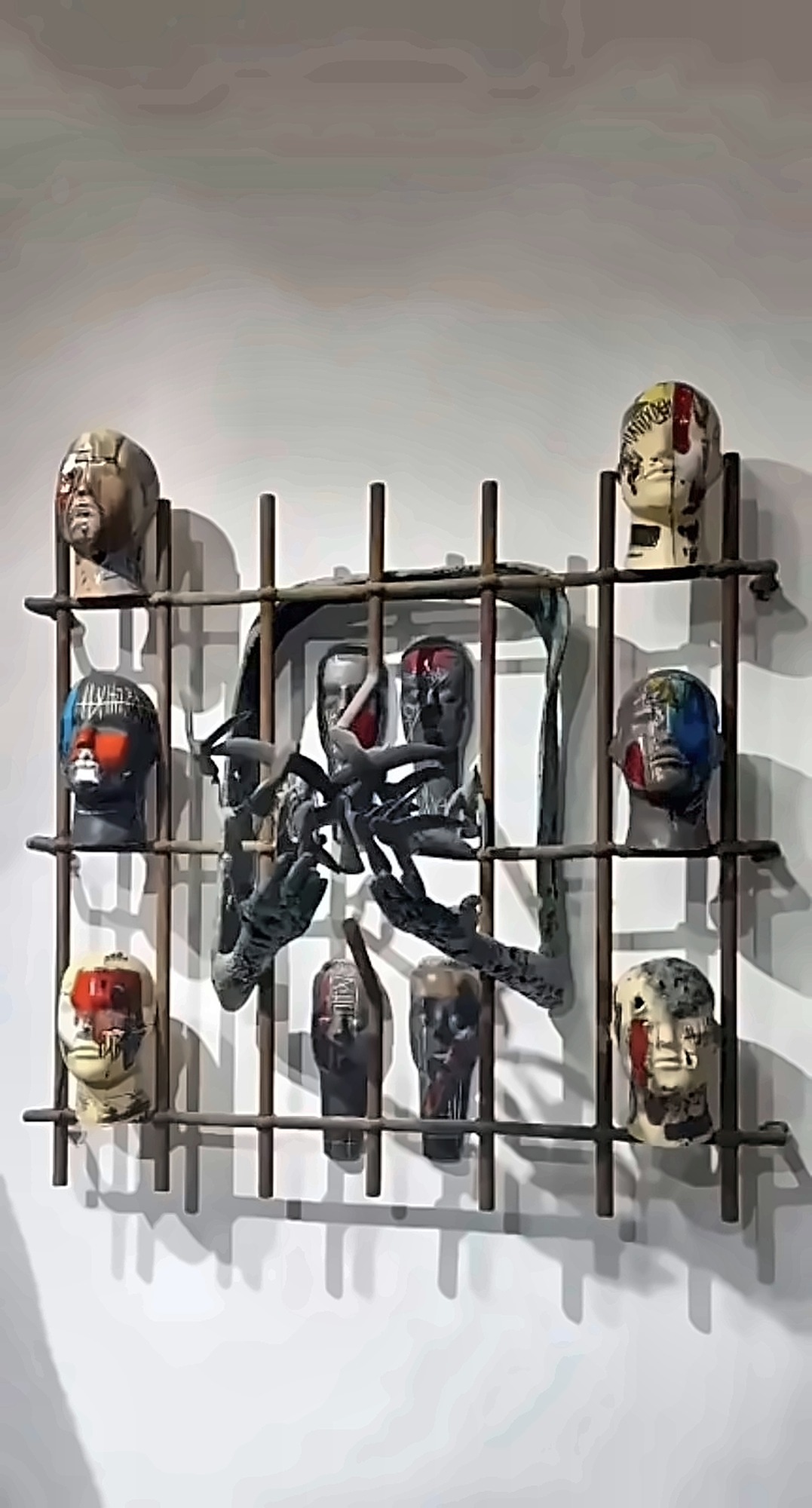 Painted ceramic heads held in a welded iron grid.