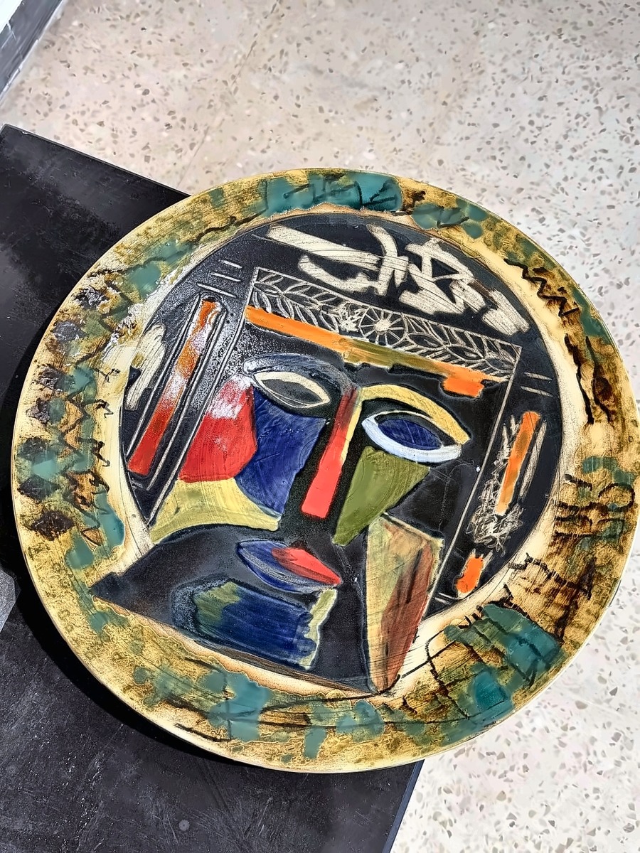 A large glazed ceramic plate with an incised face in ochre and blue.