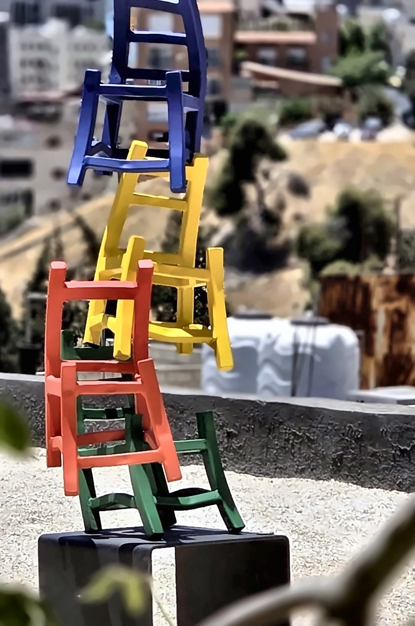 Small painted chairs stacked in a column against a view of hills.