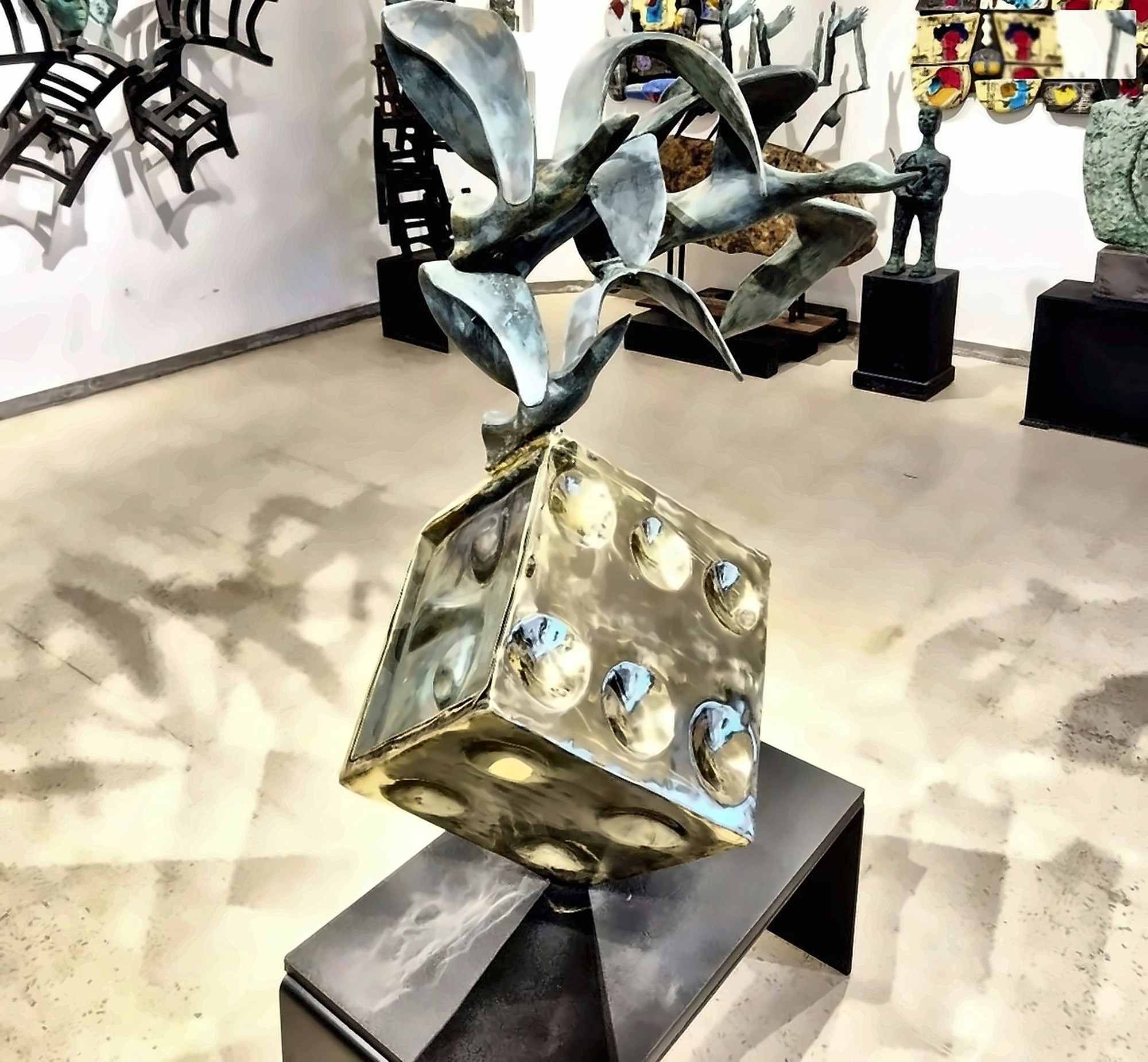 A gilded bronze die on a plinth in a gallery hung with work.