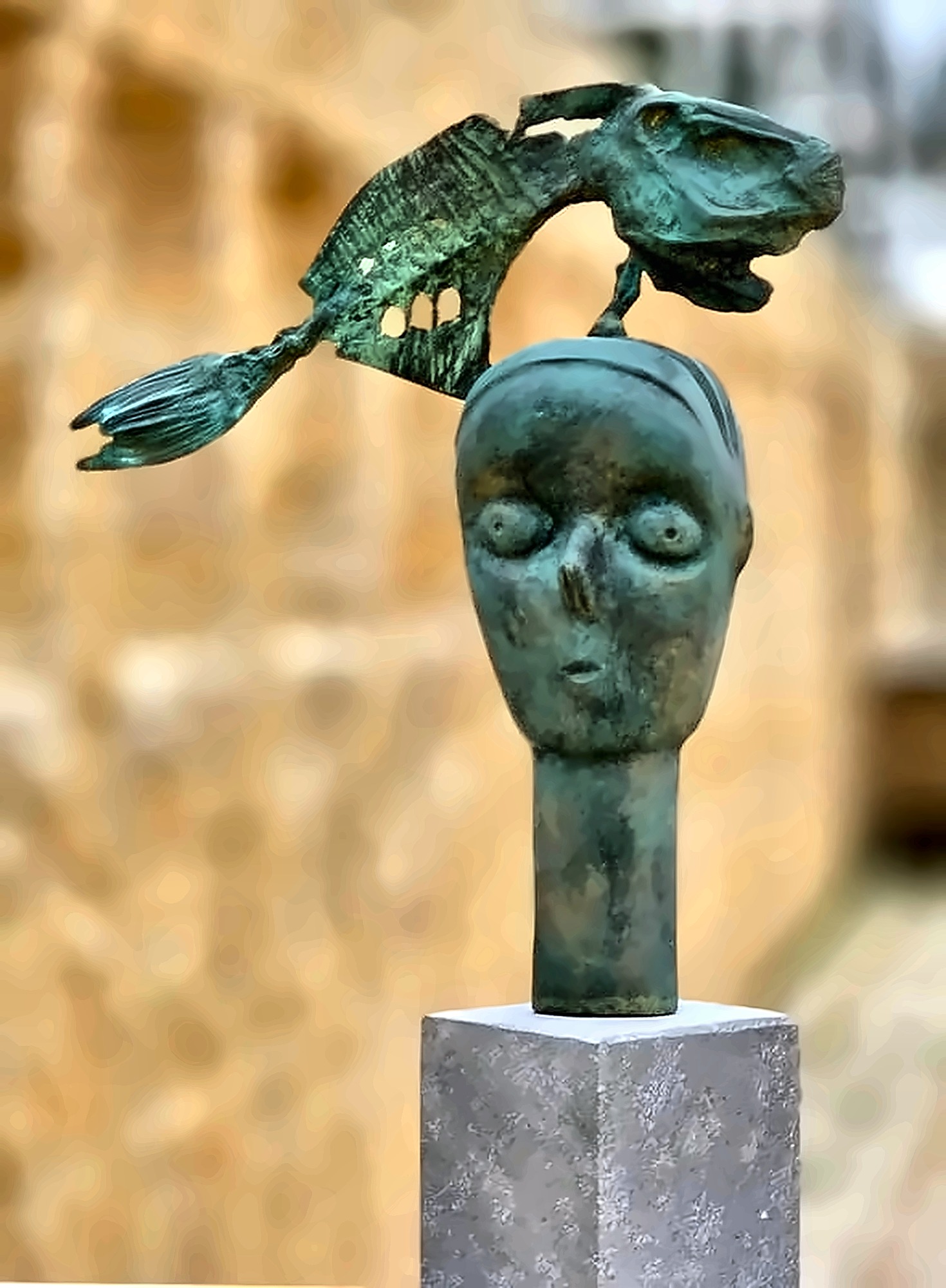 A bronze head with a large pierced fish arcing over it instead of birds.