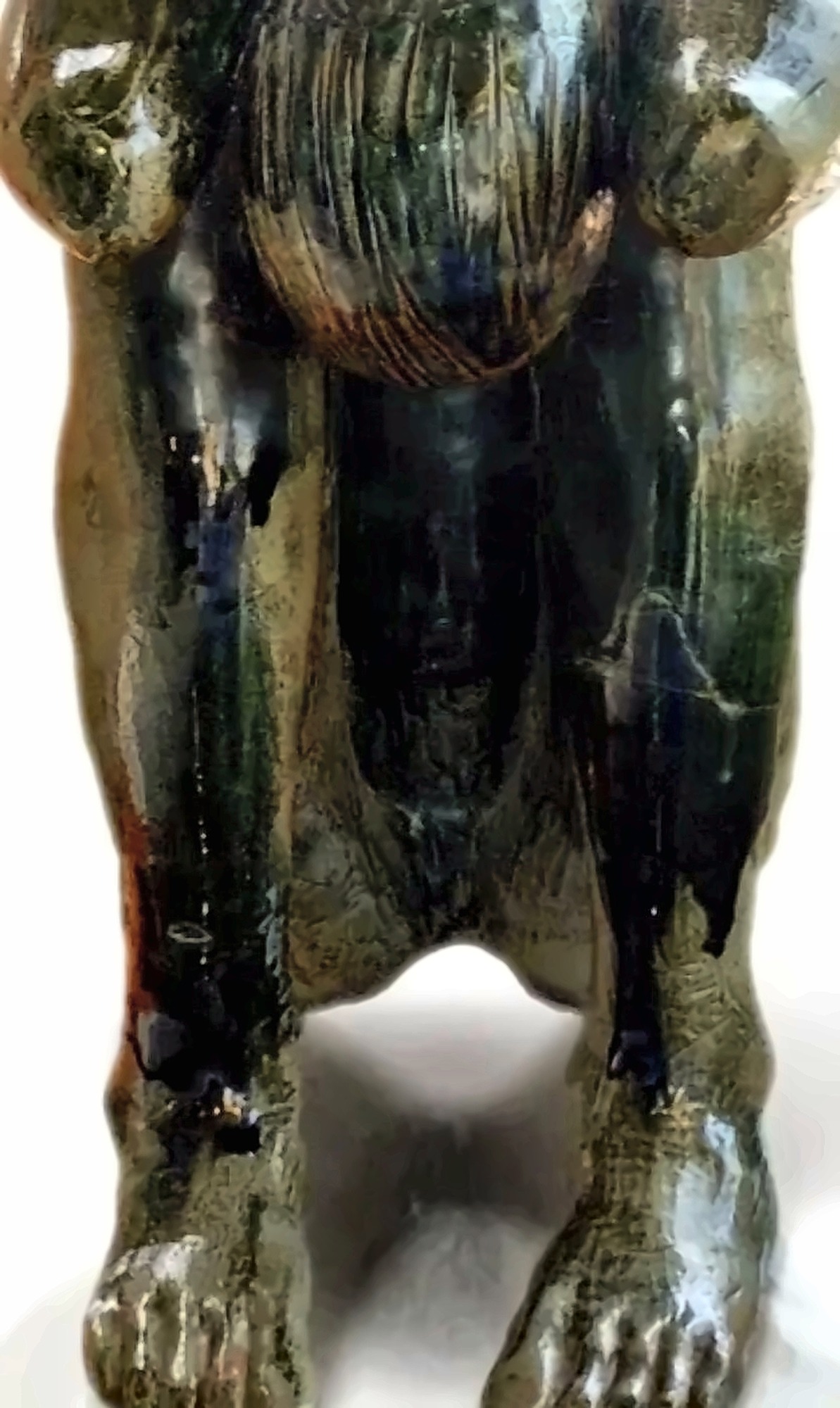 A heavy glazed ceramic figure with running ochre and green glaze.