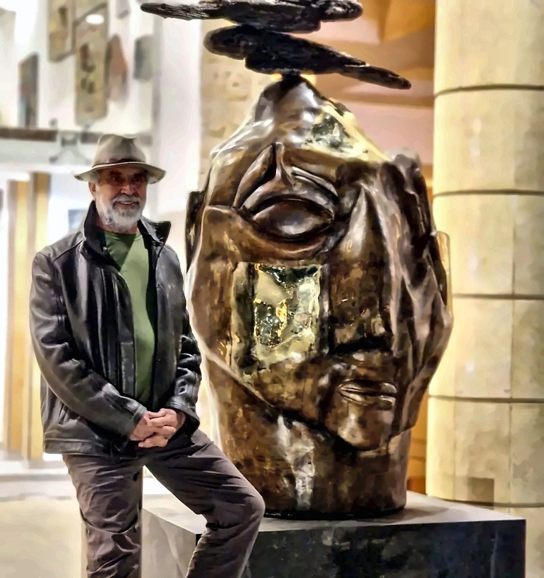 The artist standing beside a large bronze head in a hotel hall.