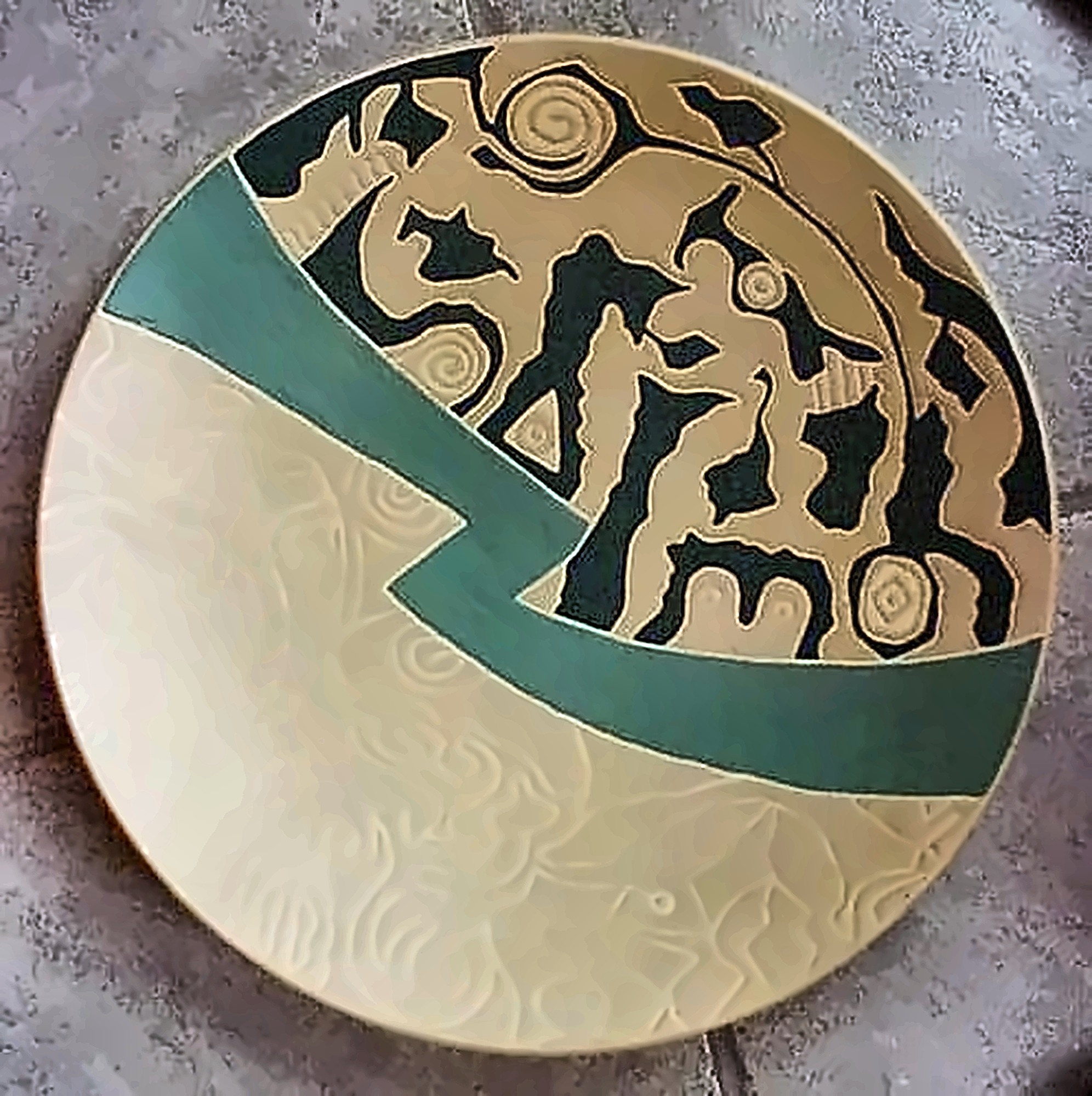 A cream plate crossed by a green band, one half incised with faint pattern, the other filled with dense black figures.