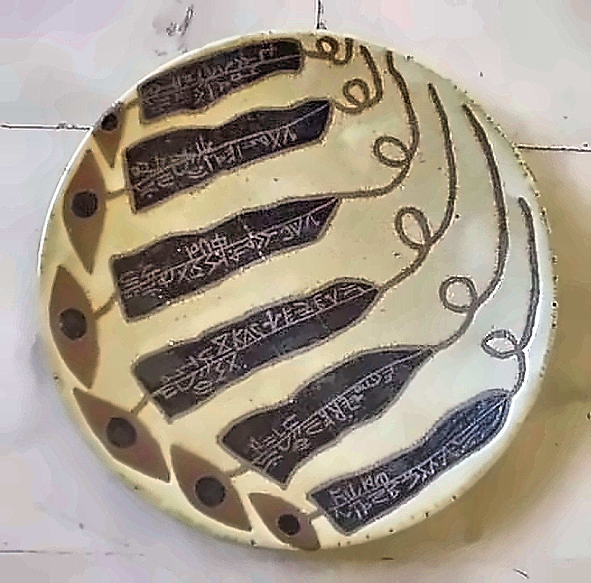 A pale plate with six dark tapering bands of incised script curving across it, a border of eyes below.