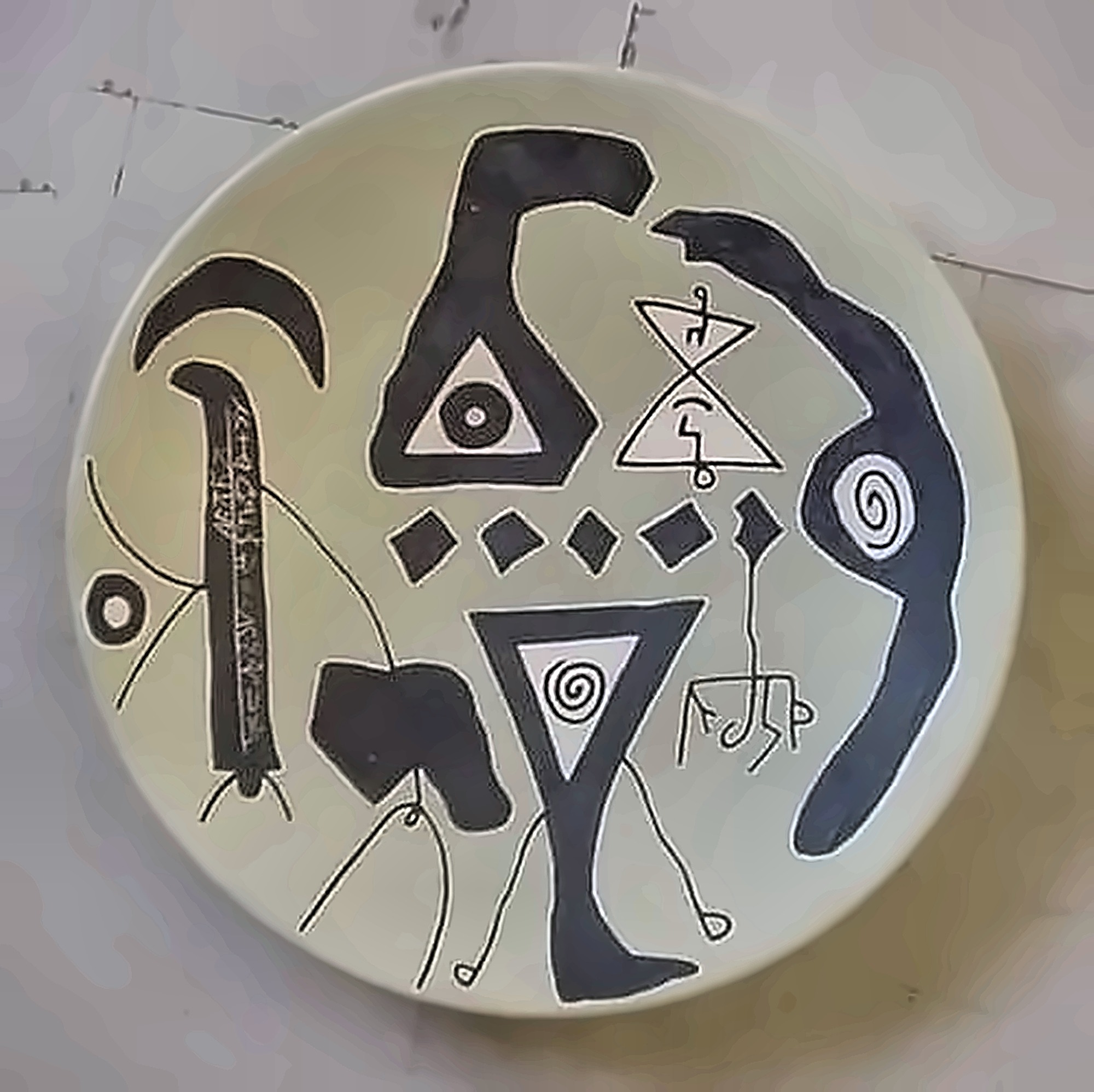 A pale plate with black hooks, triangles, spirals and a row of small diamonds.