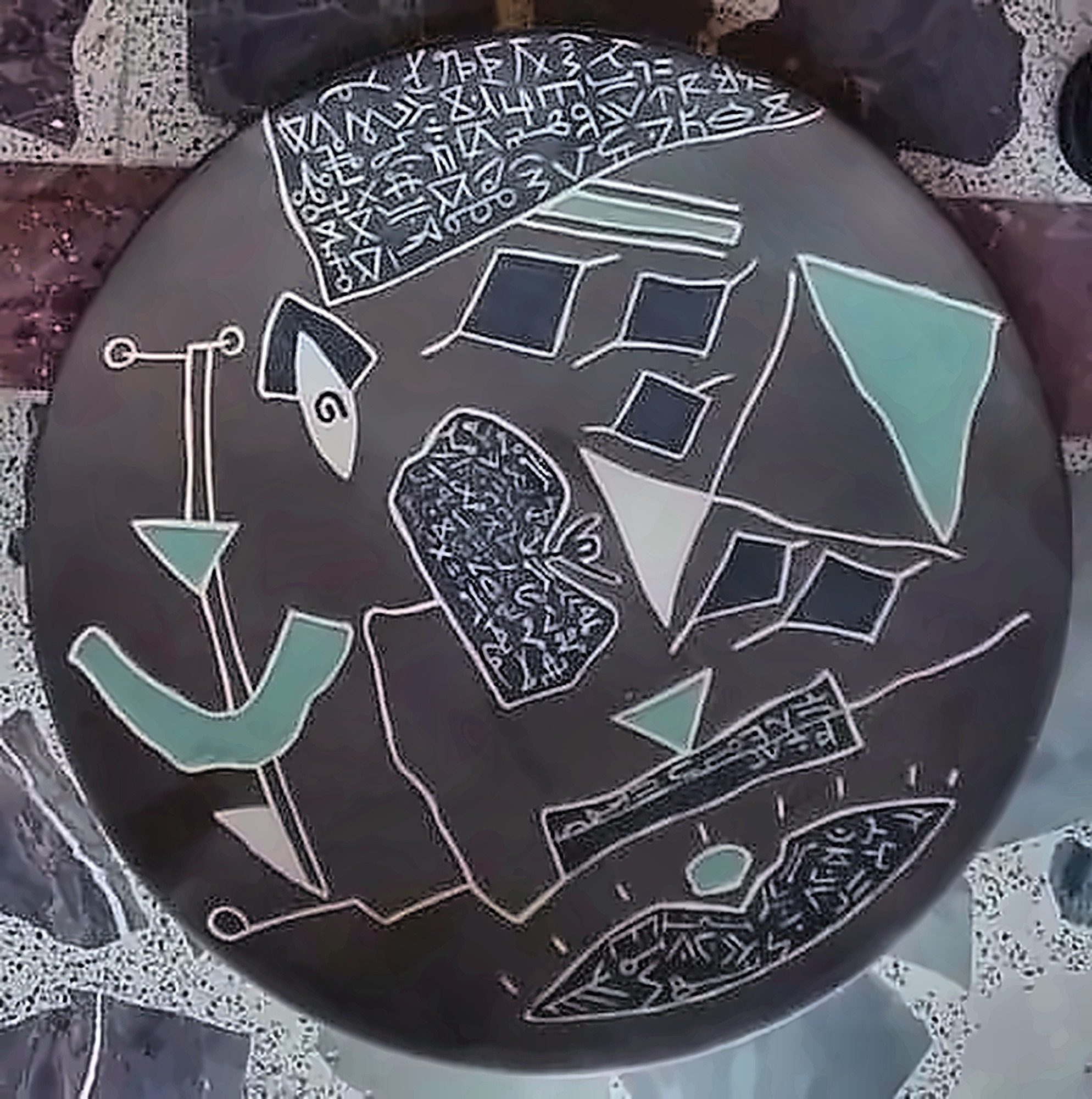 A dark grey plate with pale incised diamonds, blades and a band of script across the top, touched with turquoise.