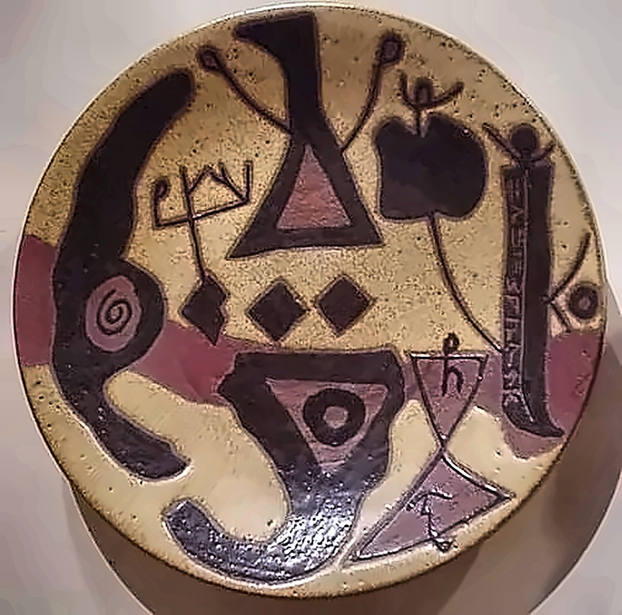 A stoneware plate with heavy black forms, a triangle, a spiral and a column of incised script down one side.