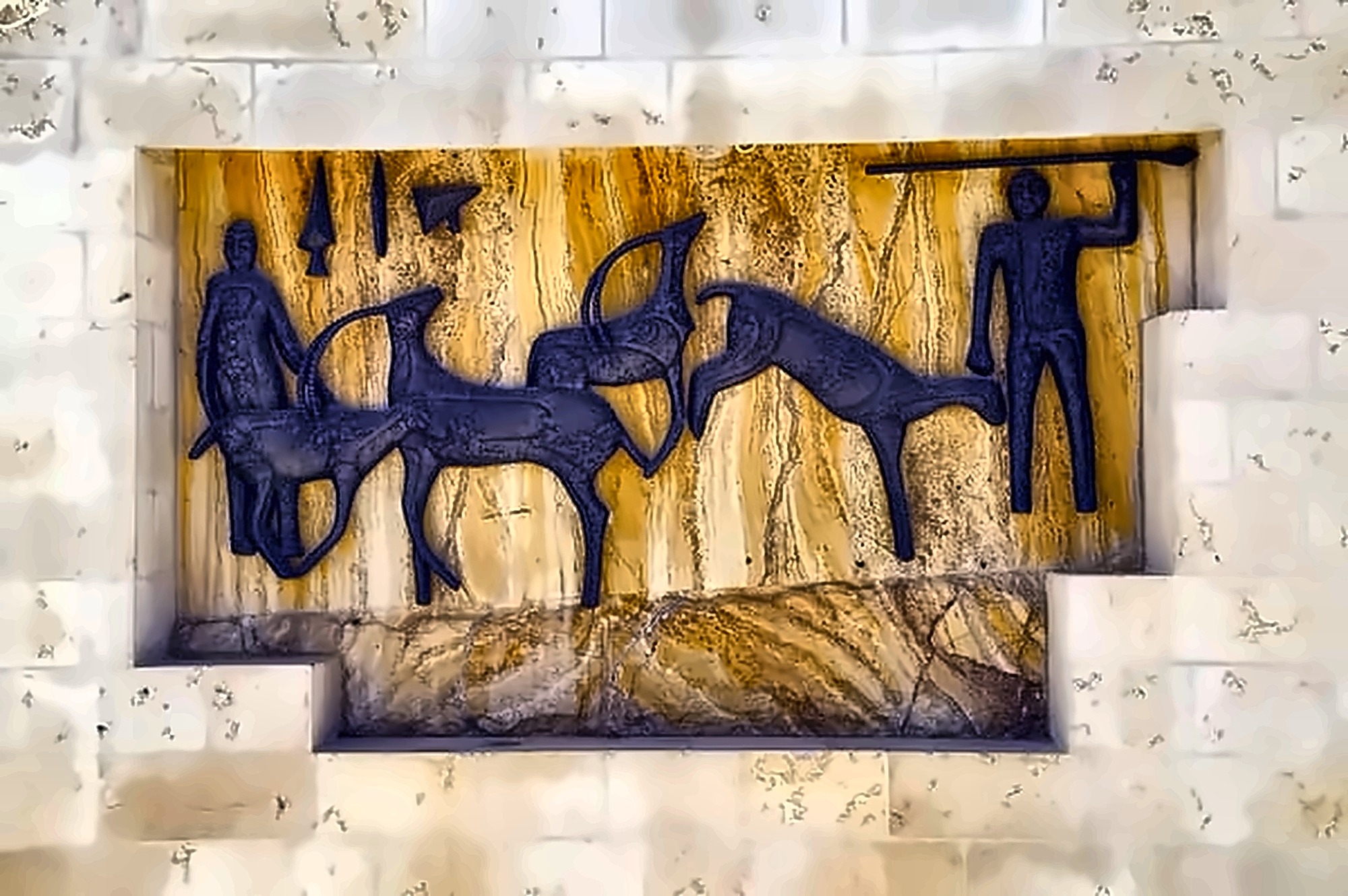 A bronze hunting relief set into a recess in a stone wall, against a ground of veined golden onyx: two figures with spears and three animals.