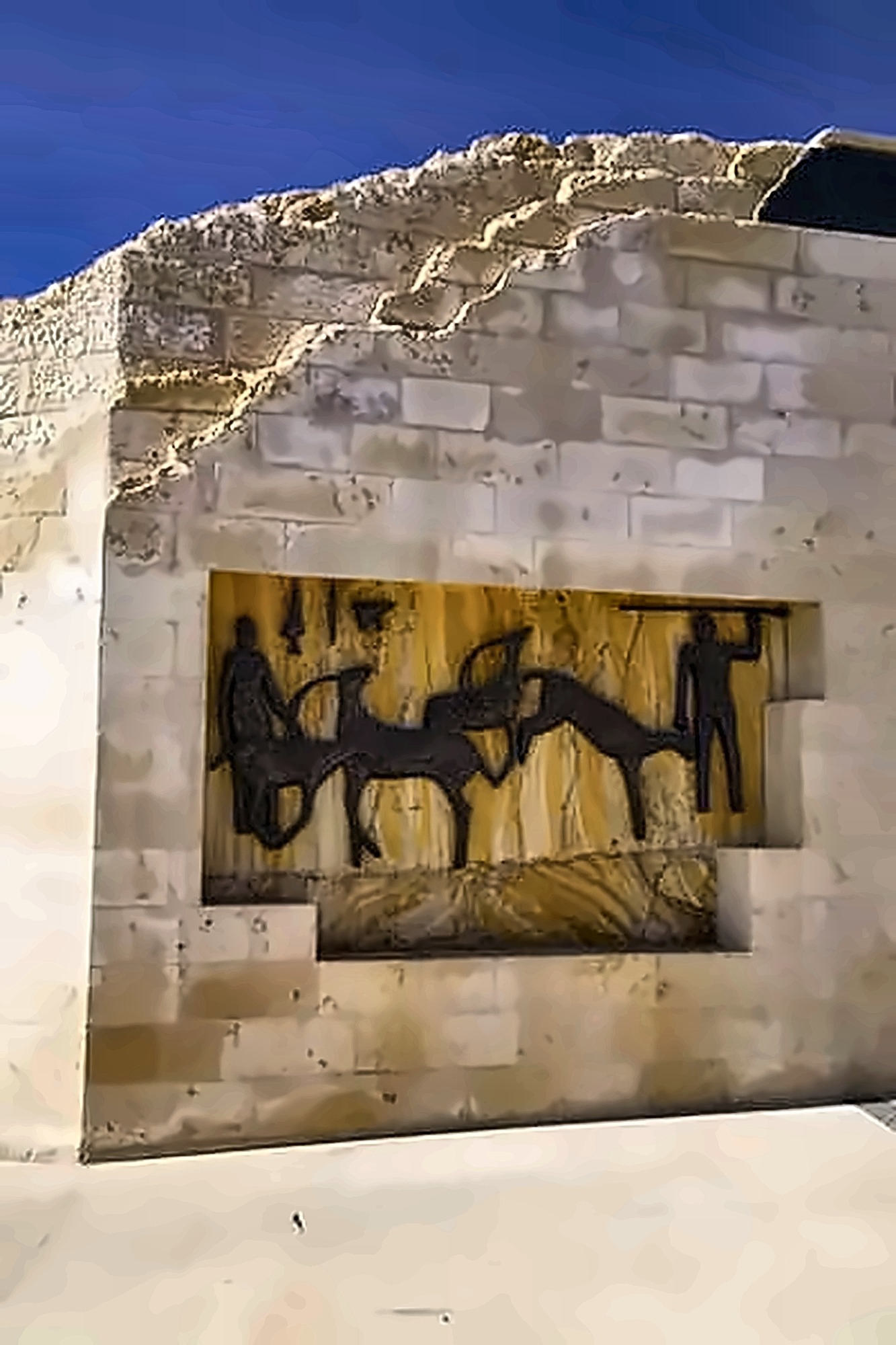 The same relief seen from further back, showing it built into the facade of a stone building under a deep blue sky.