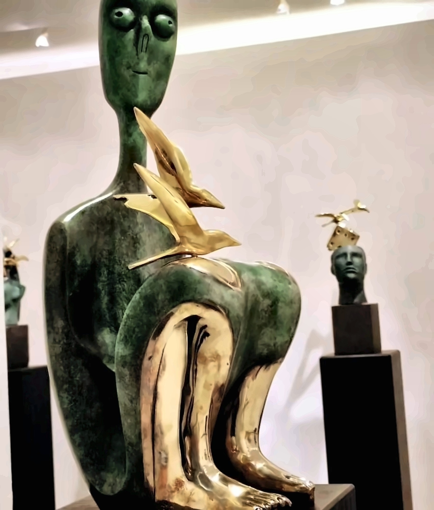 A seated green-patinated bronze figure with gilded birds at the shoulder.