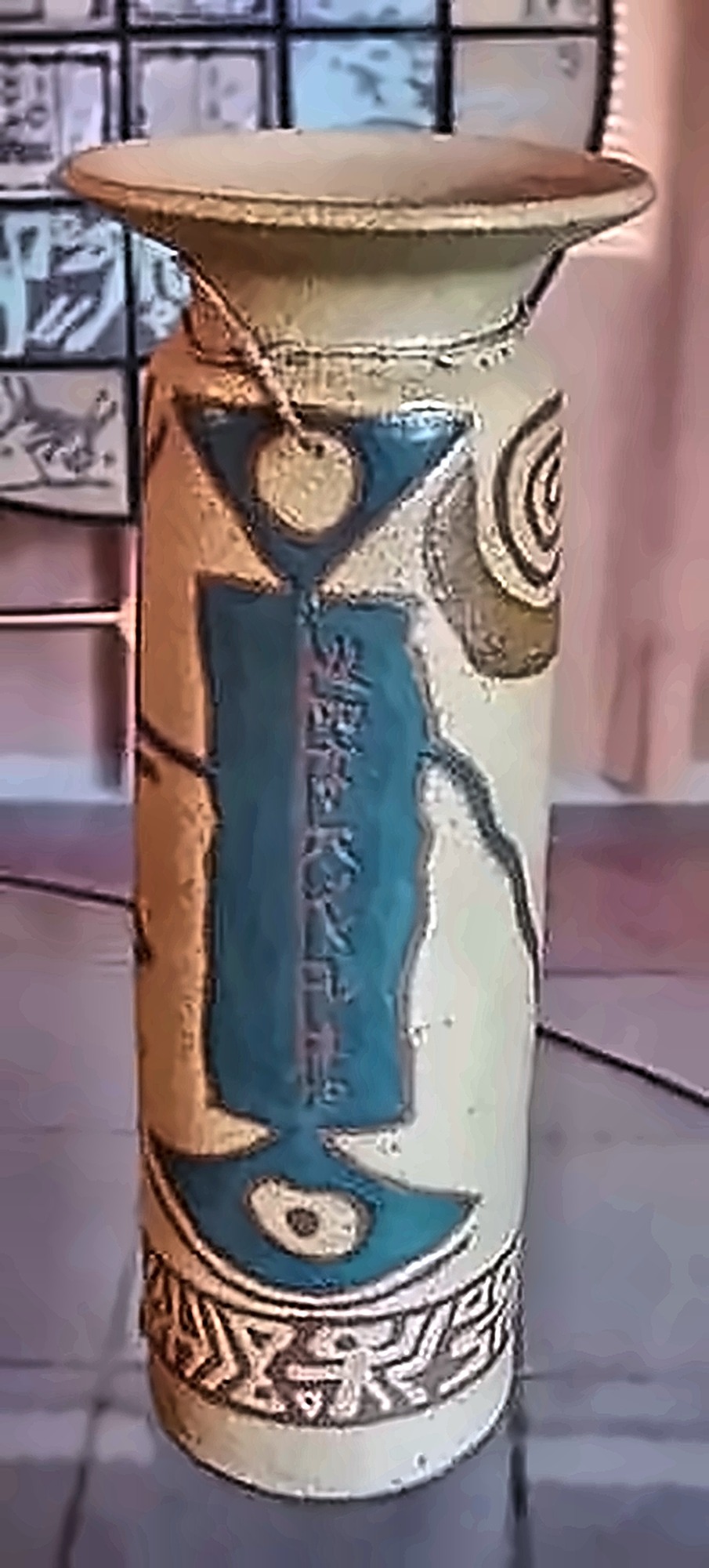 A cylindrical vase, a turquoise panel of script down its face over pale stoneware.