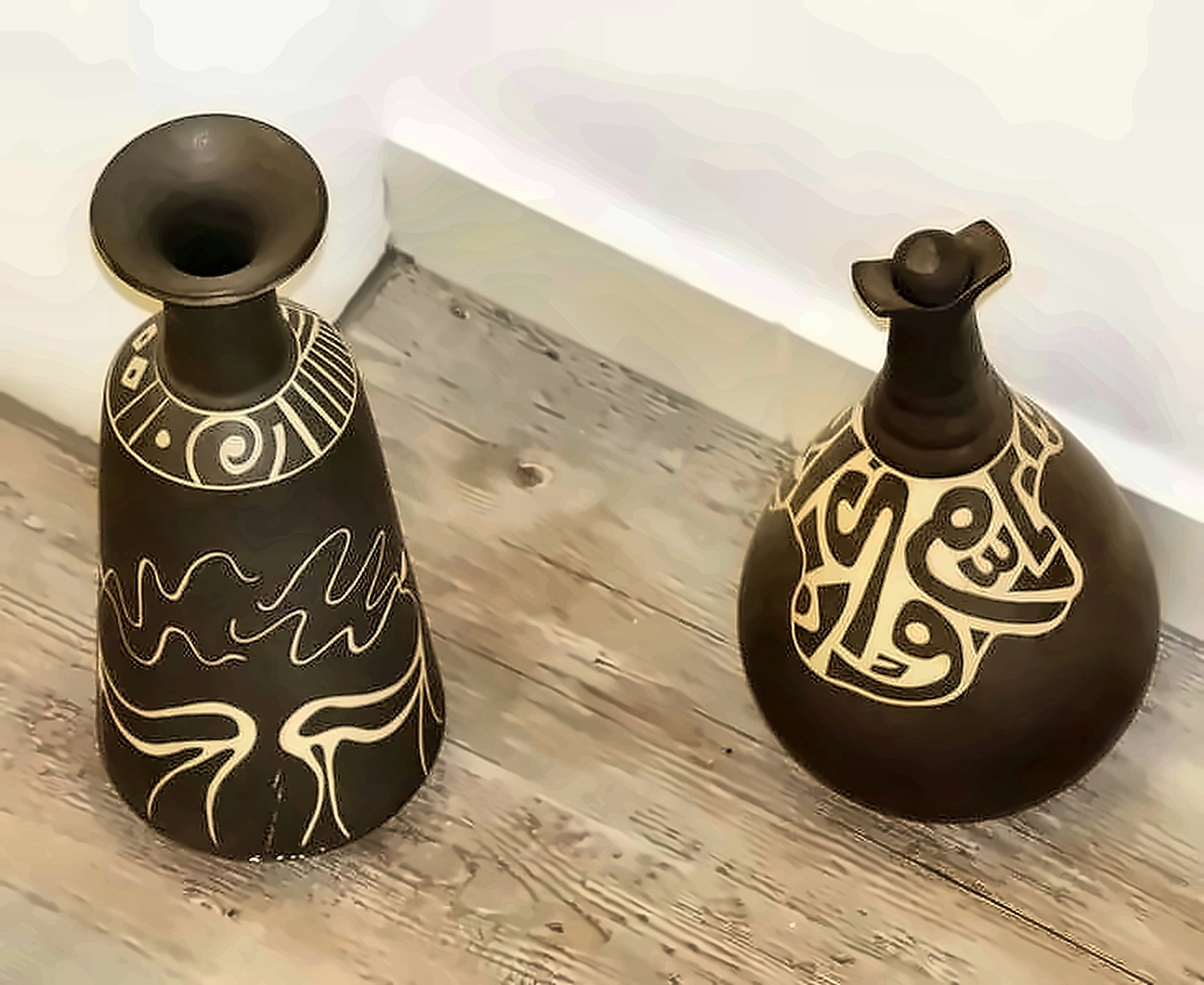 Two dark vessels, one conical and one round, cut through with white sgraffito line and script.