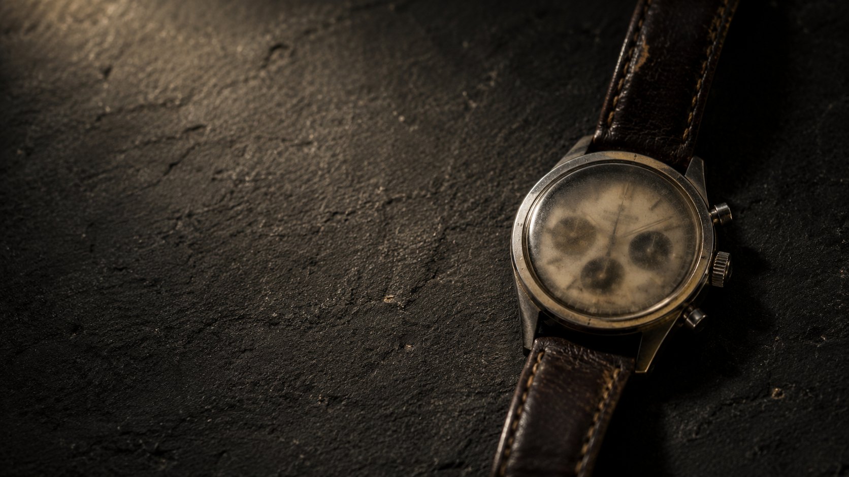 An old steel wristwatch lying on basalt.